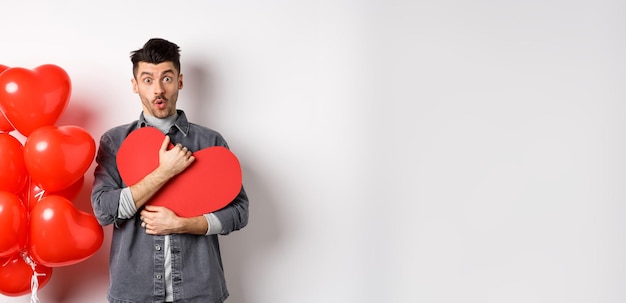 Free photo surprised man holding valentines heart card and saying wow looking amazed at camera receive secret c