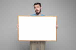 Free photo surprised man showing empty white board