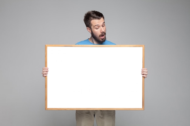 Free photo surprised man showing empty white board