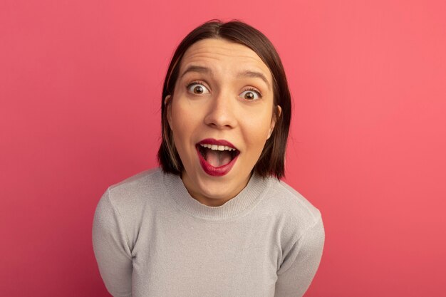 Surprised pretty caucasian woman looks at camera on pink