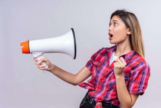 A surprised pretty young woman in checked shirt holding megaphone