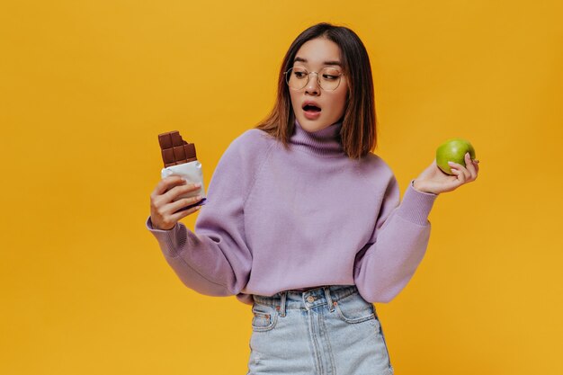 Surprised shirt-haired girl in eyeglasses looks at milk chocolate bar