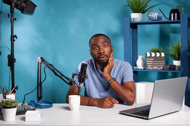 Surprised vlogger interacting with audience recieved shocking question during online live broadcast session using laptop. Shocked influencer talking with fanbase in recording studio sitting at desk.