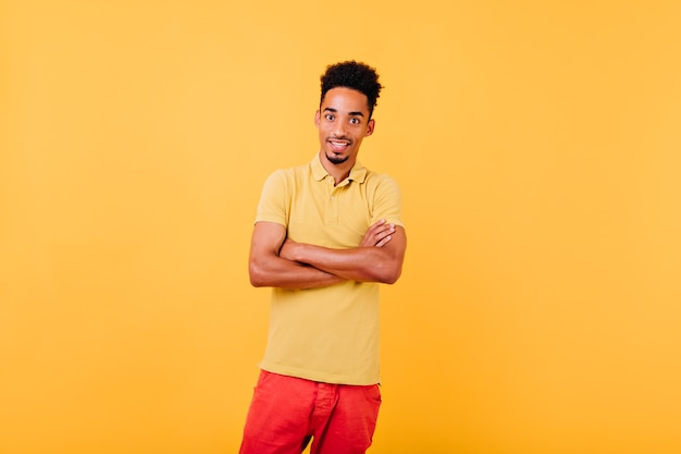 Surprised well-dressed african model posing with arms crossed. Indoor shot of amazed man standing in confident pose.