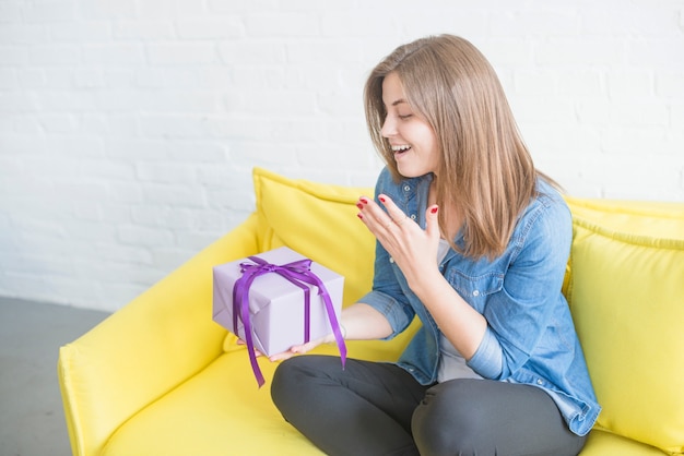 Surprised woman sitting on sofa holding gift