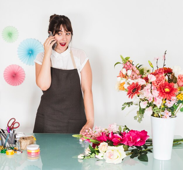 Surprised woman talking on smartphone with bunch of flowers on desk