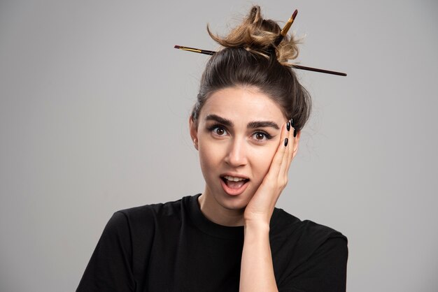 Surprised woman with messy bun standing on gray wall. 