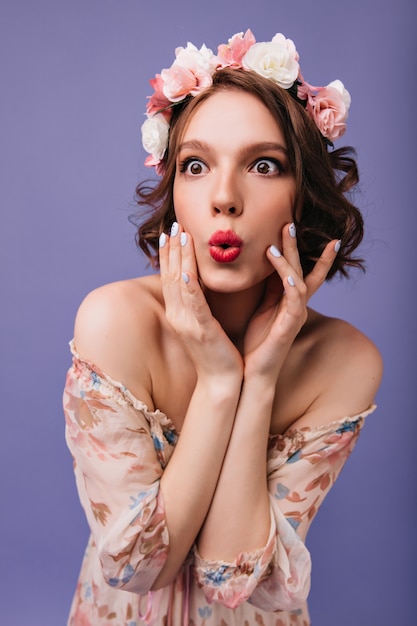 Surprised woman with stylish makeup and manicure posing. Indoor phofo of amazed girl in circlet of flowers isolated.