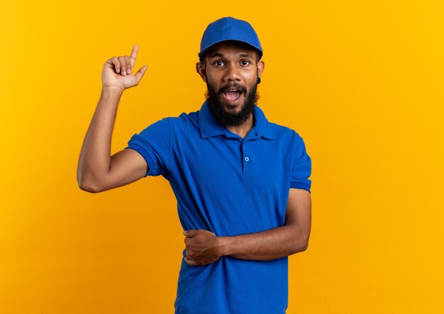 Surprised young afro-american delivery man pointing up isolated on orange background with copy space