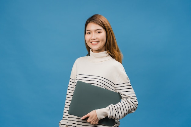 Surprised young Asia lady hold laptop with positive expression, smile broadly, dressed in casual clothing and looking at front on blue wall