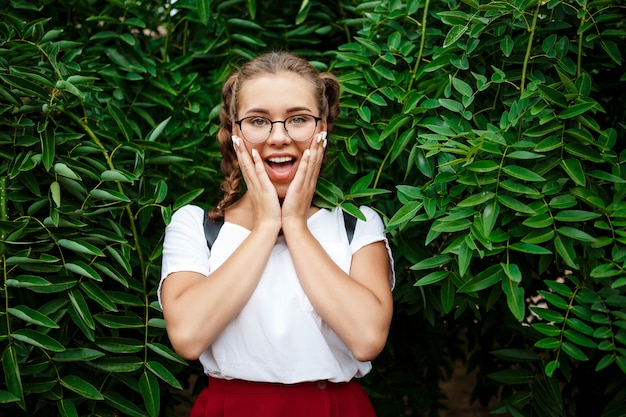 Free Photo surprised young beautiful female student in glasses posing over leaves outdoors.