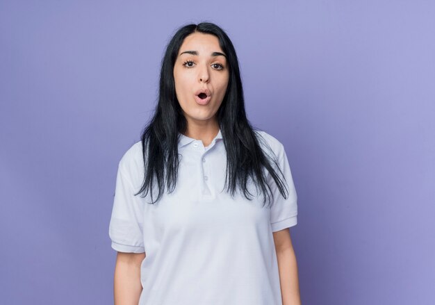 Surprised young brunette caucasian girl stands isolated on purple wall