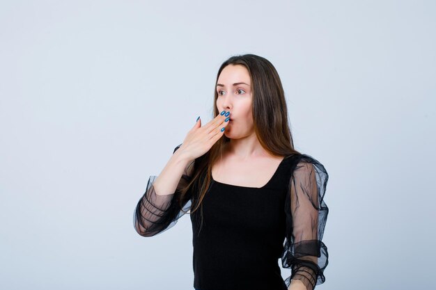 Surprised young girl is looking away by holding hand on mouth on white background