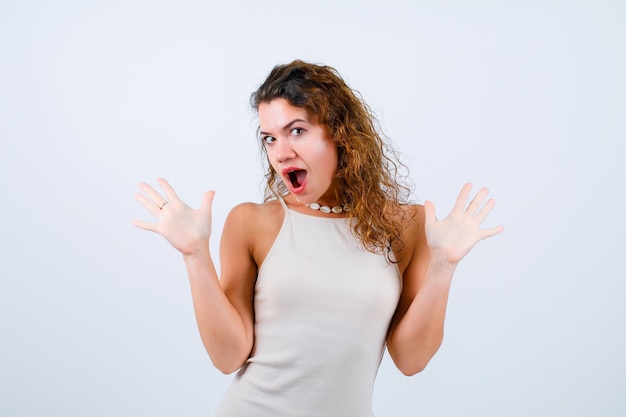 Surprised young girl is looking at camera by opening wide her hands on white background