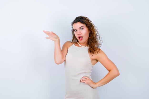 Surprised young girl is looking up and putting hand on waist on white background