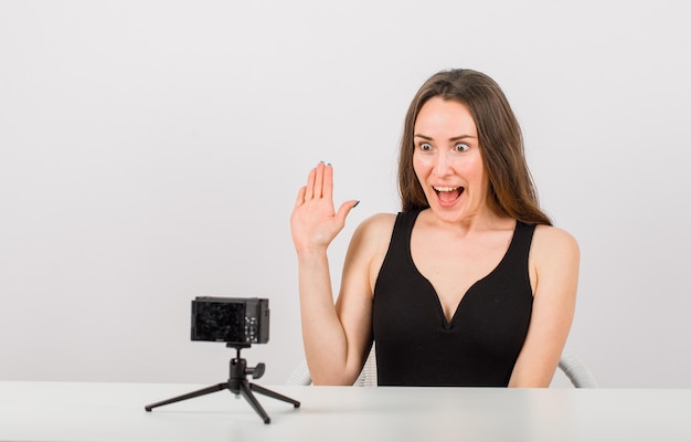 Free photo surprised young girl is posing at little camera by showing hi gesture on white background