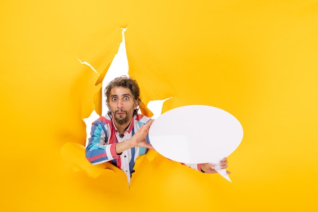 Free Photo surprised young guy pointing white page with free space in a torn hole in yellow paper