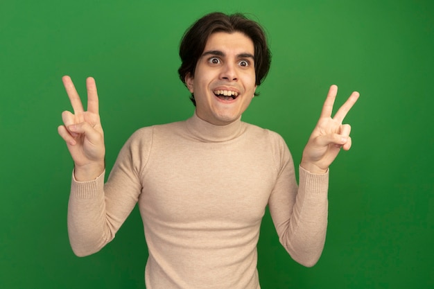 Free Photo surprised young handsome guy showing peace gesture isolated on green wall