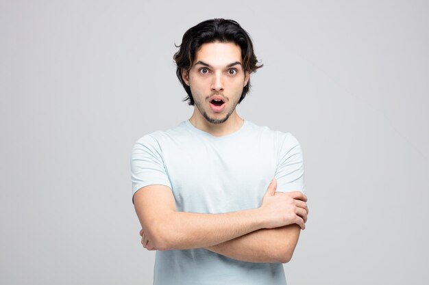 surprised young handsome man standing with crossed arms looking at camera isolated on white background