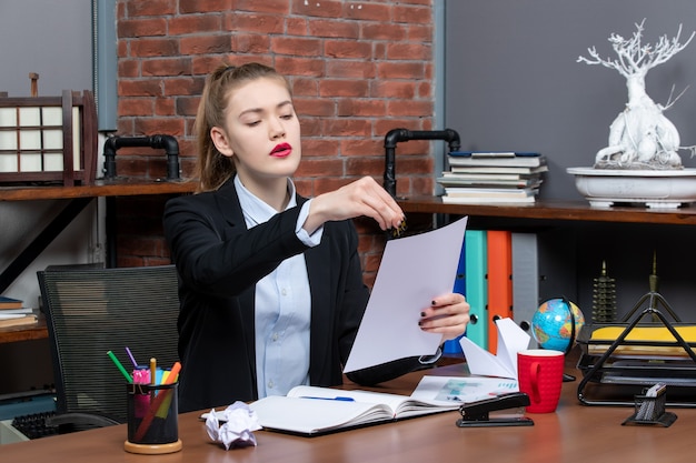 Surprised young lady sitting at a table and reading her notes in notebook in the office