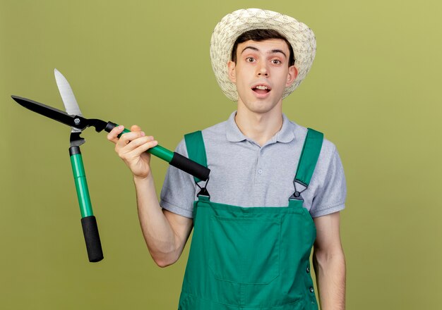 Surprised young male gardener wearing gardening hat holds clippers