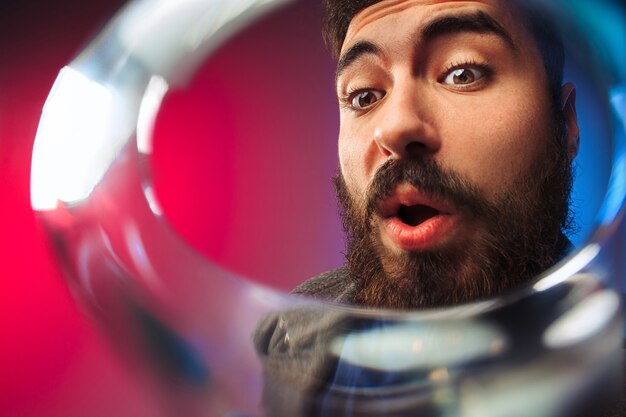 The surprised young man in party clothes posing with glass of wine.