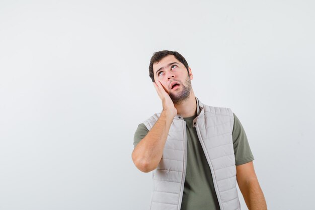 Surprised young man putting his left hand on his cheek on white background