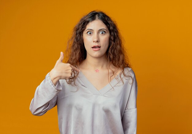 Surprised young pretty girl points at herself isolated on yellow wall