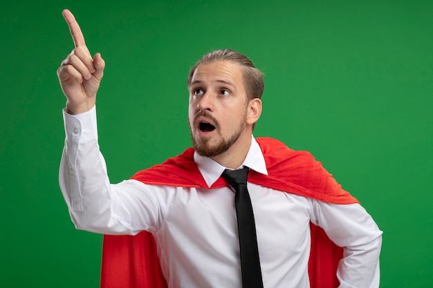 Free photo surprised young superhero guy wearing tie points at side isolated on green background