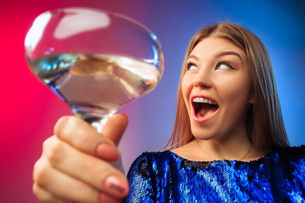 The surprised young woman in party clothes posing with glass of wine. Emotional female cute face. View from the glass