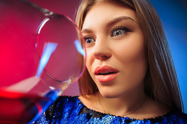 The surprised young woman in party clothes posing with glass of wine