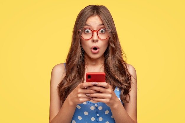 Surprised young woman with glasses posing against the yellow wall