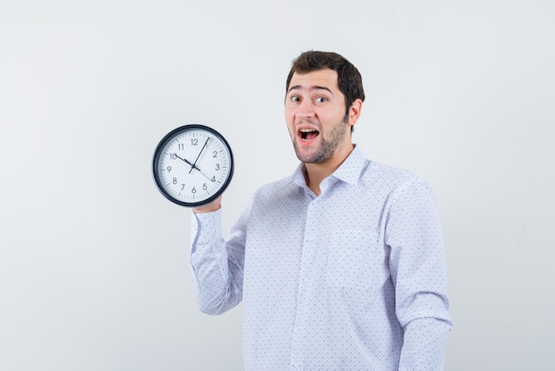 Surprising young man holding an oclock on his hand on white background