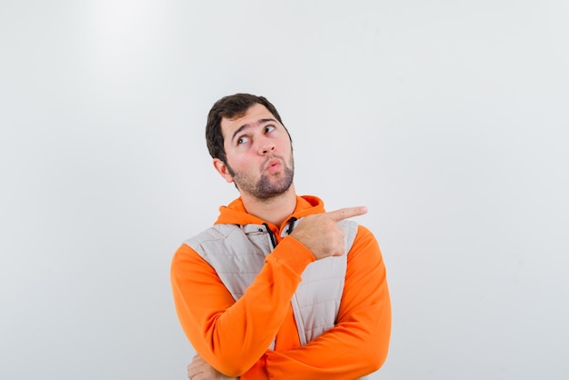 Surprising young man pointing something with fingers on the right on white background