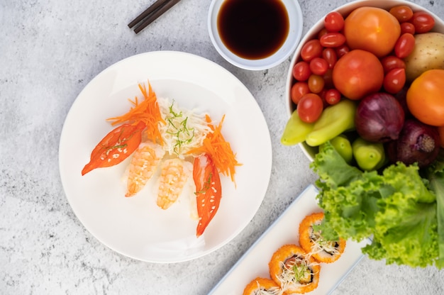 Sushi is in a plate with chopsticks and dipping sauce on a white cement floor.