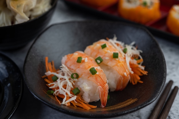 Sushi is in a plate with chopsticks and dipping sauce on a white cement floor.