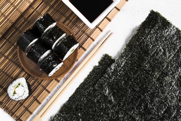 Sushi rolls and soy sauce on bamboo mat near seaweed