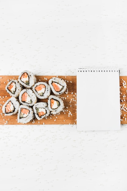 Free Photo sushi rolls and spiral notepad on wooden tray with splatter of uncooked rice on white backdrop