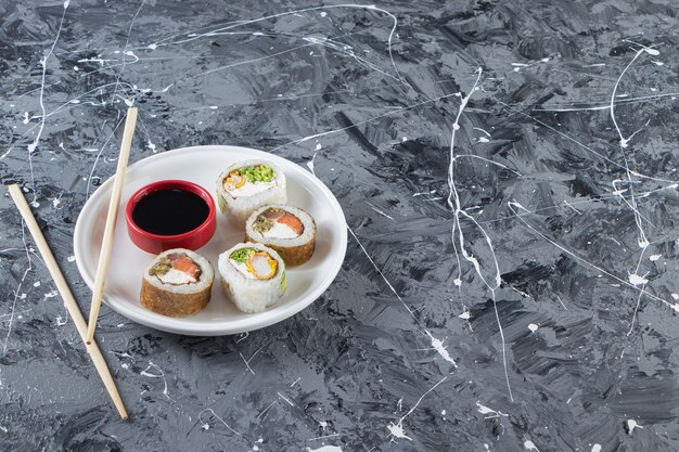 Sushi rolls with soy sauce placed on a white plate with chopsticks . 