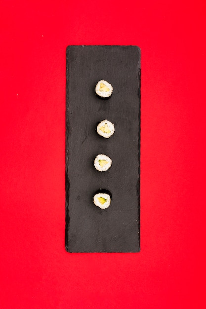 Free Photo sushi with cucumber arranged in row on black slate tray over red background