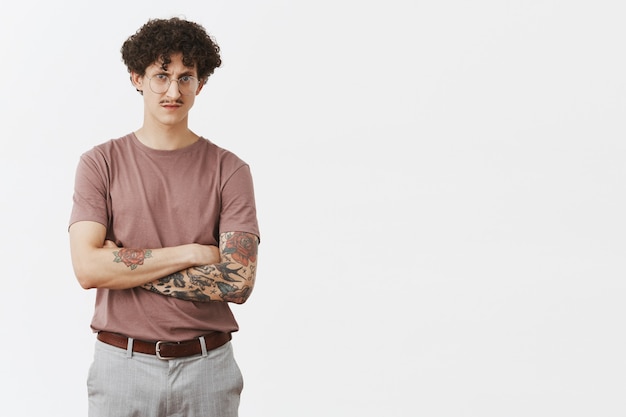 Free photo suspicious concerned attractive jewish man with curly hairstyle and moustache frowning crossing hands on chest staring with disbelief and disappointment over gray wall