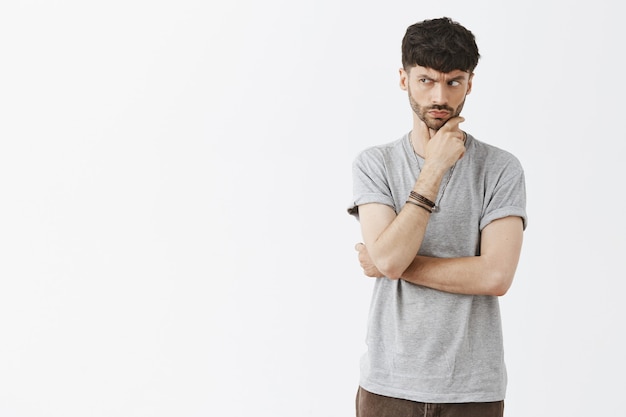 Suspicious and thoughtful handsome guy posing against the white wall