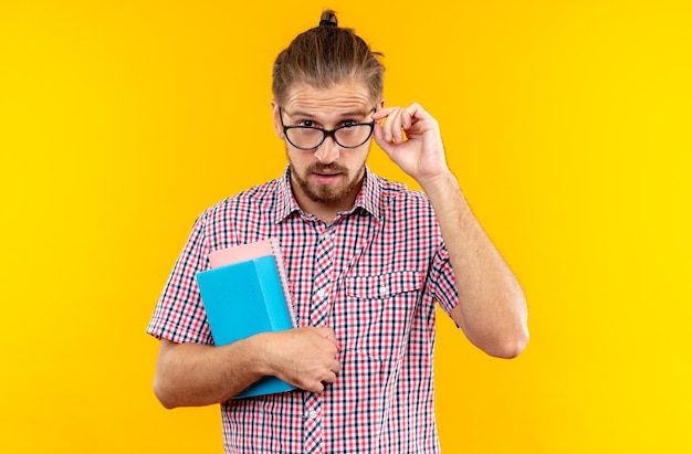 Free photo suspicious young guy student wearing backpack with glasses holding book isolated on orange wall