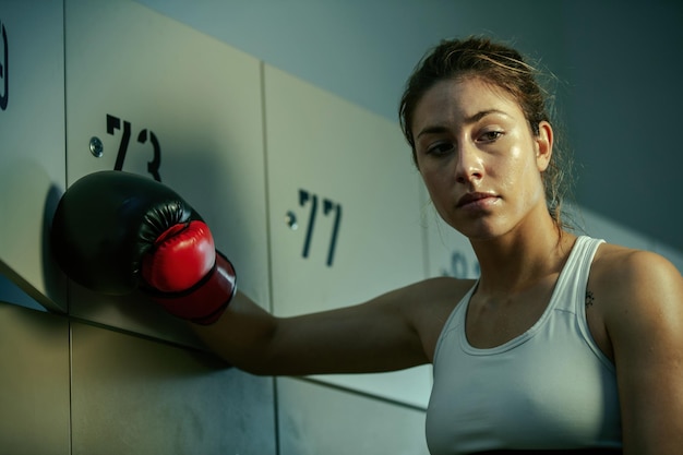 Free photo sweaty athletic woman thinking of something in gym's dressing room after boxing training