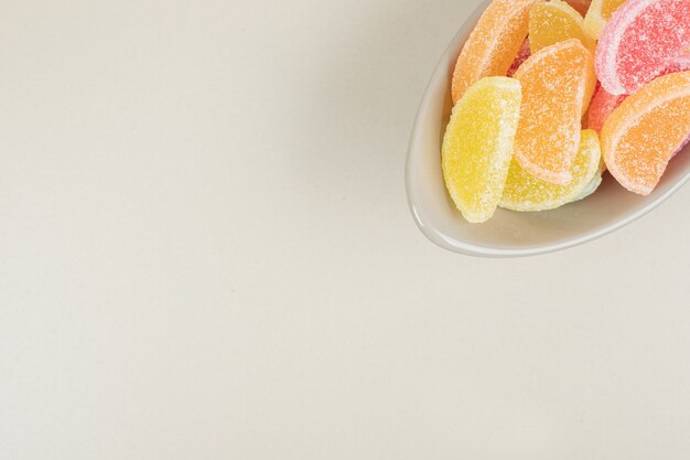 Sweet colorful jelly candies in bowl on beige surface