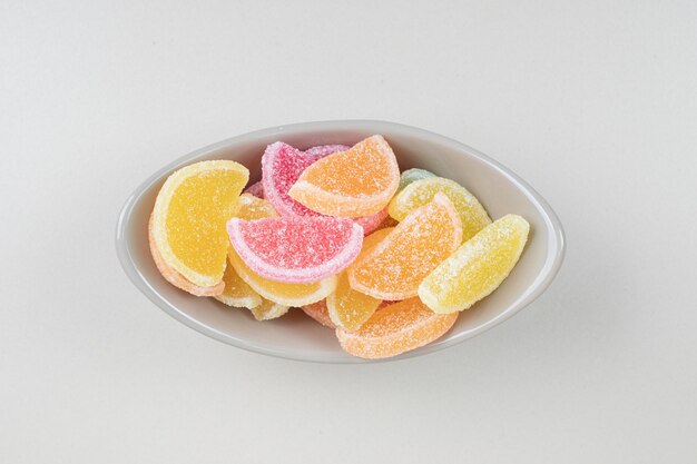 Sweet colorful jelly candies in bowl on beige surface