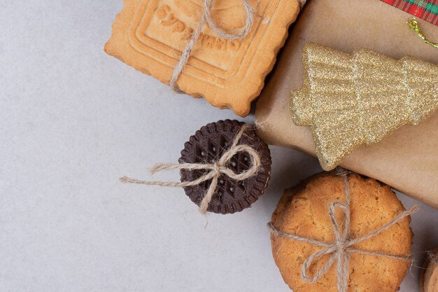 Sweet cookies in rope with gift and Christmas golden toy on white surface