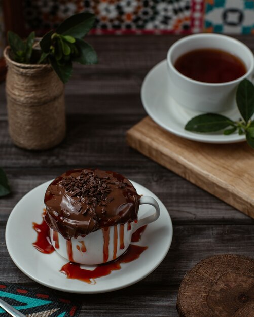 A sweet cup of tasty chocolate mousse with strawberry syrup inside served with a cup of tea