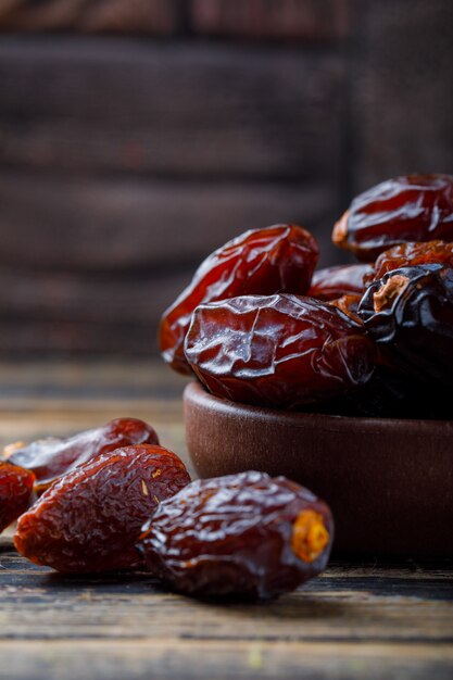 Sweet dates in a clay plate on stone tile and wooden background, close-up.