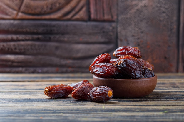 Sweet dates in a clay plate on stone tile and wooden background